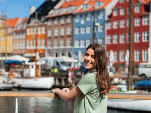 Lachelnde junge Touristin, die am Nyhavn Hafenpier in Kopenhagen sitzt hallo auf Danisch skrivanek