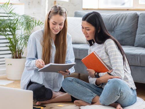 Two young girls learning foreign languages sitting on the floor at home Anglicisms skrivanek