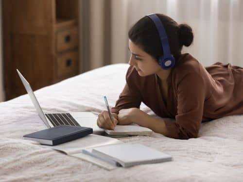 Eine Frau arbeitet mit Laptop und Kopfhorern im Bett schwerste sprache der welt skrivanek