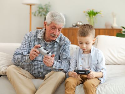 Ein Großvater und sein Enkelsohn sitzen auf dem Sofa und spielen Videospiele mit Game Controllern wer hat das erste videospiel erfunden übersetzungsbüro berlin