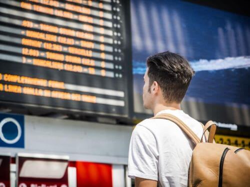 Junger Mann mit Rucksack schaut auf Abfahrtsanzeige ubersetzungsbüro skrivanek