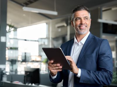 Glücklicher Geschäftsmann mittleren Alters der einen Anzug trägt und im Büro steht und ein Tablet benutzt glokalisierung übersetzungsbüro berlin