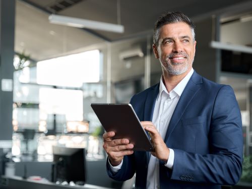 Glucklicher Geschaftsmann mittleren Alters der einen Anzug tragt und im Buro steht und ein digitales Tablet benutzt glokalisierung ubersetzungsburo berlin