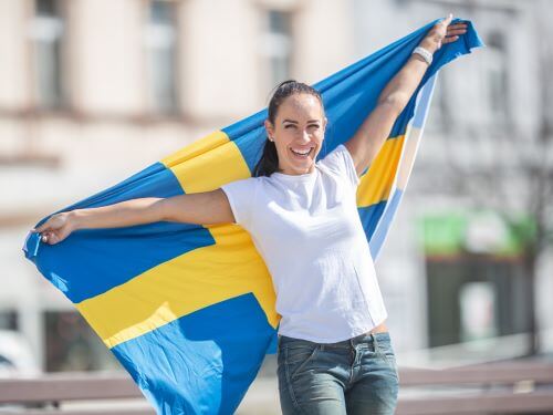 Lachelnde Frau halt schwedische Flagge auf einer Straße auswandern nach schweden ubersetzungsburo berlin