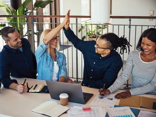 Eine Gruppe von lachelnden jungen Geschaftsleuten, die sich bei der Arbeit an einem Burotisch die Hande reiche auswandern nach Kanada ubersetzungsburo Berlin
