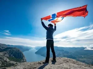 Person mit Norwegen Flagge auf Felsplateau Symbol furs Auswandern nach Norwegen Ubersetzungsburo Berlin
