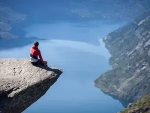 Person sitzt auf Trolltunga mit Blick auf Fjord Auswandern nach Norwegen Ubersetzungsburo Berlin