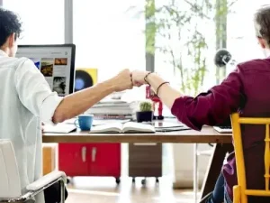 Zwei Kollegen geben sich im Buro einen Fist Bump eine alternative Geste zum High Five Emoji Ubersetzungsburo Berlin